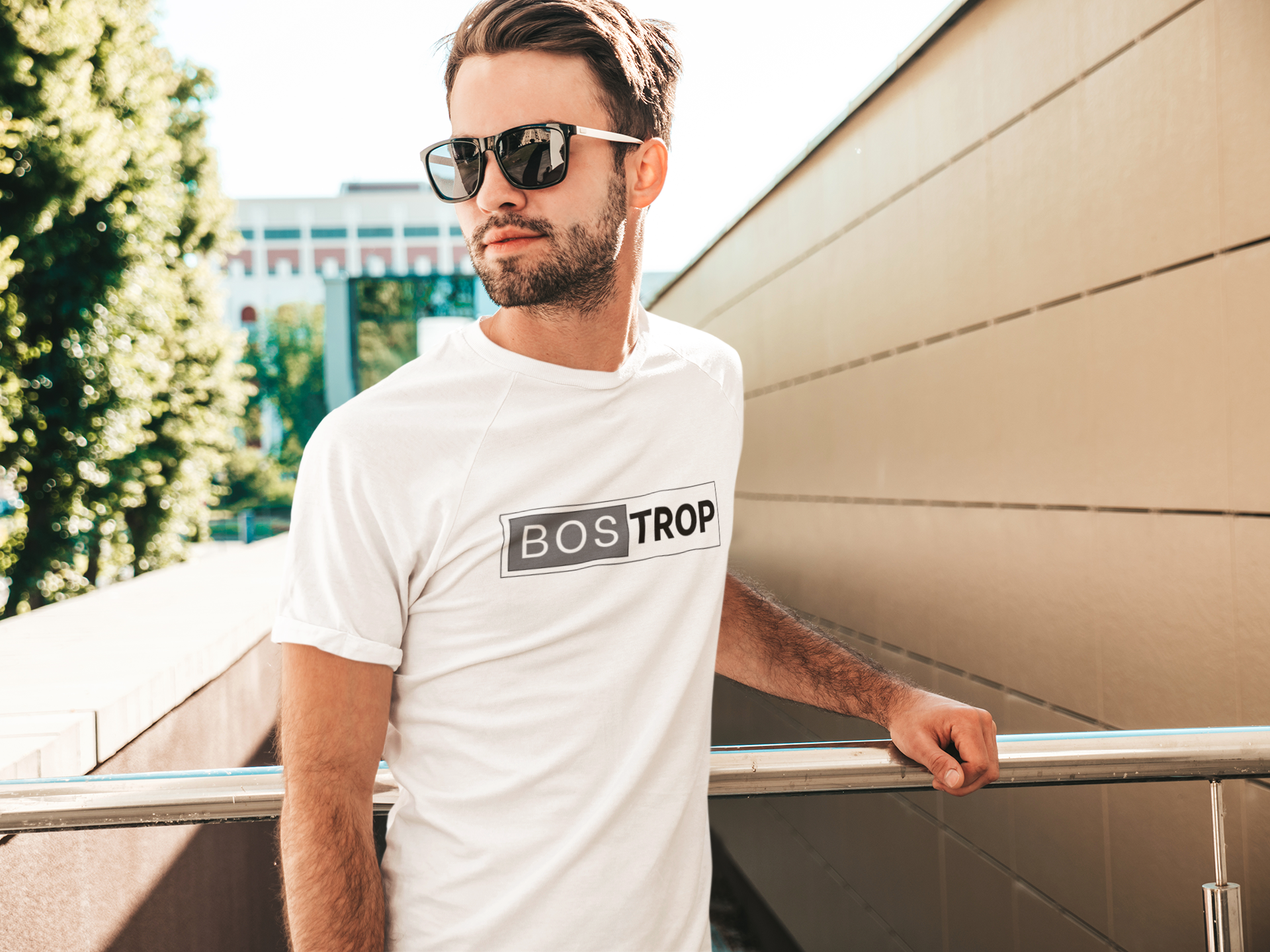 Man wearing a white t-shirt with 'BOS TROP' logo, standing outdoors.